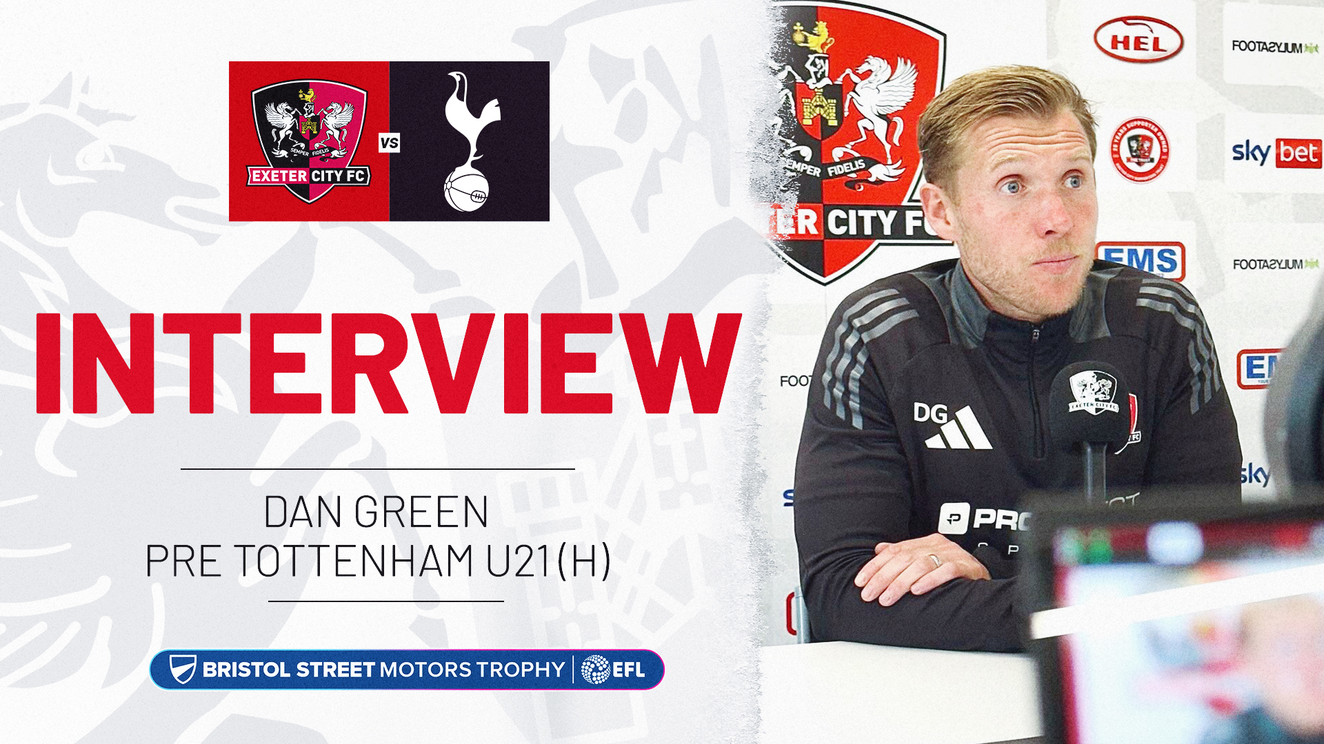 Interview graphic. On the right is an image of Dan Green, wearing a black coaches tracksuit, talking into a mic, on the left is text reading: INTERVIEW / DAN GREEN PRE TOTTENHAM U21 (H). The Bristol Street Motors Trophy Logo is below the text.